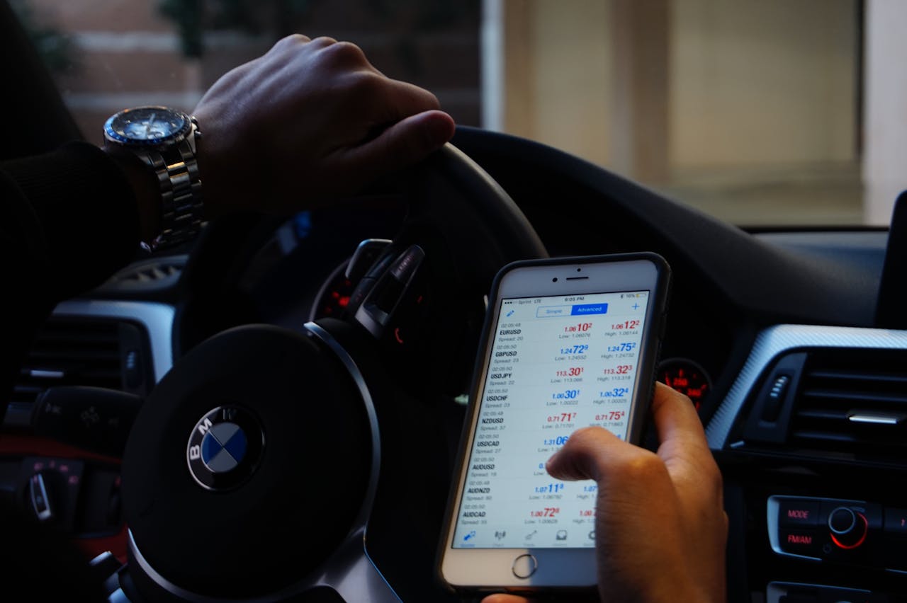 Person using mobile phone for currency trading while driving BMW car.