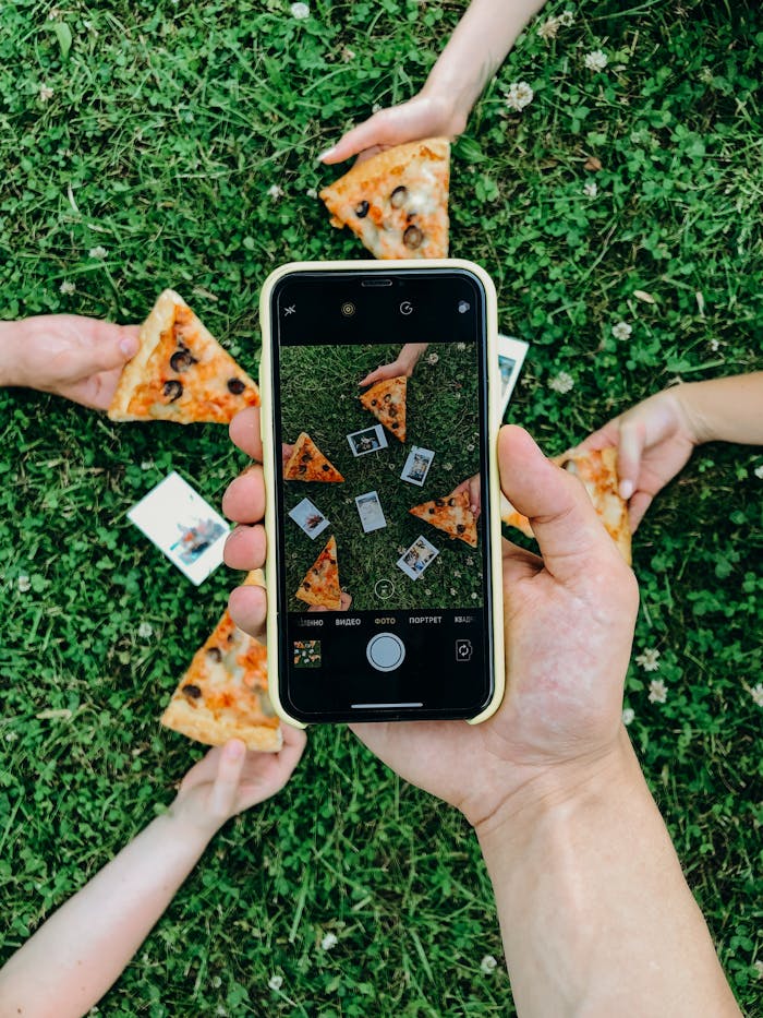 Top view of a picnic setting with hands holding pizza slices captured on a smartphone camera.